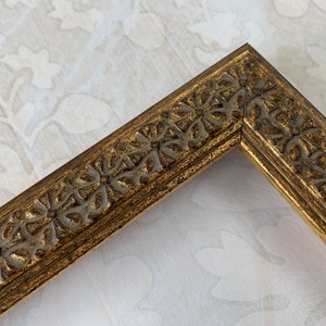 May include: A gold picture frame with a decorative, ornate design. The frame has a raised, textured pattern of leaves and flowers.