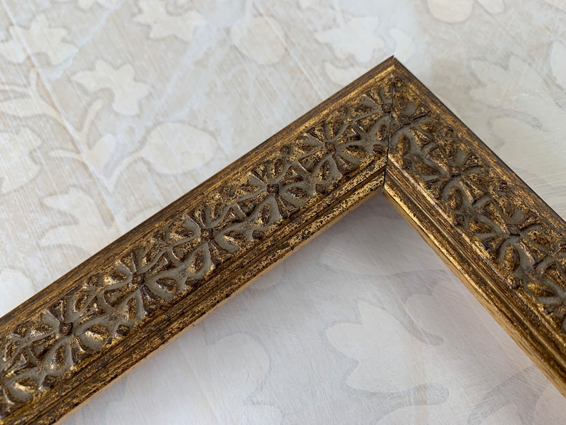May include: A gold picture frame with a decorative, ornate design. The frame has a raised, textured pattern of leaves and flowers.