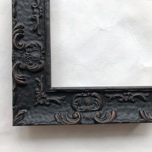 May include: Black ornate picture frame with a detailed, carved design. The frame is made of wood and has a distressed finish.