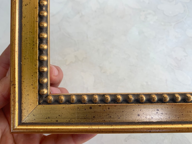 May include: Gold picture frame with a beaded edge. The frame has a distressed, antique look.