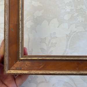 May include: A wooden picture frame with a gold trim. The frame is brown with a slightly reddish hue.