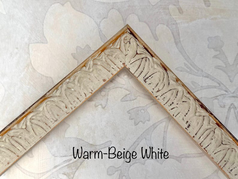 May include: A corner of a warm-beige white picture frame. The frame has a carved, ornate design with a distressed finish. The text "Warm-Beige White" is displayed in a black font.