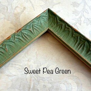 May include: A corner of a Sweet Pea Green picture frame. The frame has a distressed finish with carved leaf details. The frame is a muted green color with hints of brown. The text "Sweet Pea Green" is written in a script font.