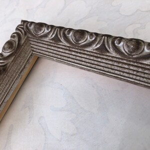 May include: A silver picture frame with an ornate design. The frame has a distressed finish and is made of wood.