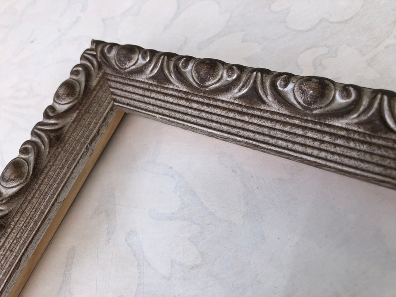 May include: A silver picture frame with an ornate design. The frame has a distressed finish and is made of wood.