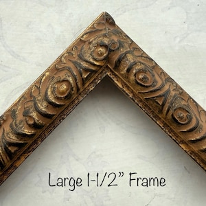 May include: A corner section of a decorative picture frame. The frame is a warm brown color with ornate, raised detailing in a darker brown and gold. The text "Large 1-1/2" Frame" is visible.