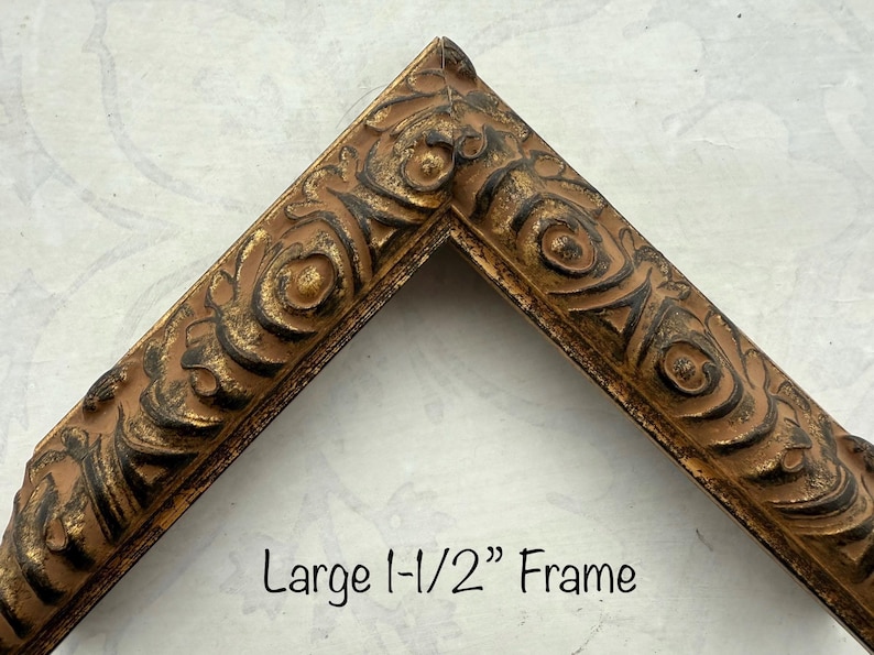 May include: A corner section of a decorative picture frame. The frame is a warm brown color with ornate, raised detailing in a darker brown and gold. The text "Large 1-1/2" Frame" is visible.