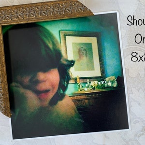 May include: A framed photograph of a young person with dark hair, looking down, with a blue wall and a framed picture in the background. The text "Shown On 8x8" is printed on the white border of the photo.