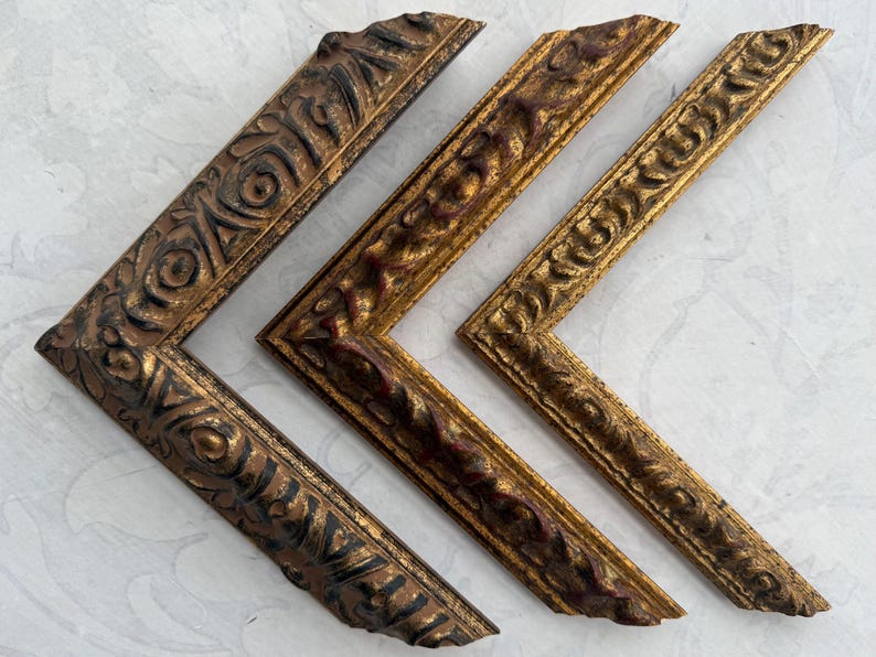May include: Three ornate picture frames in gold, black, and red tones. The frames are all different sizes and have intricate designs. The frames are arranged in a triangular shape with the largest frame at the bottom and the smallest frame at the top.