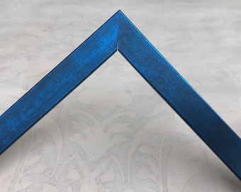 May include: A corner section of a picture frame featuring a vibrant blue finish with a subtle, brushed metallic texture. The frame is joined at a sharp forty-five-degree angle, creating a clean, pointed peak at the top of the structure.