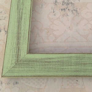 May include: A green wooden picture frame with a distressed finish. The frame has a simple design with a smooth surface.