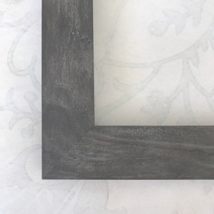 May include: Close-up of a corner of a dark gray wood picture frame.