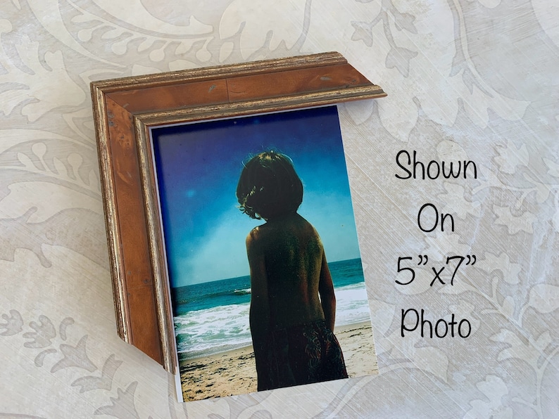 May include: A wood picture frame with a gold trim, shown on a 5" x 7" photo of a person standing on a beach.