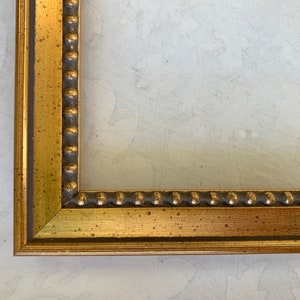 May include: A gold picture frame with a beaded edge. The frame has a distressed finish and is made of wood.