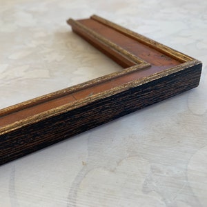 May include: A black and gold picture frame with a wood grain finish. The frame has a simple, classic design.