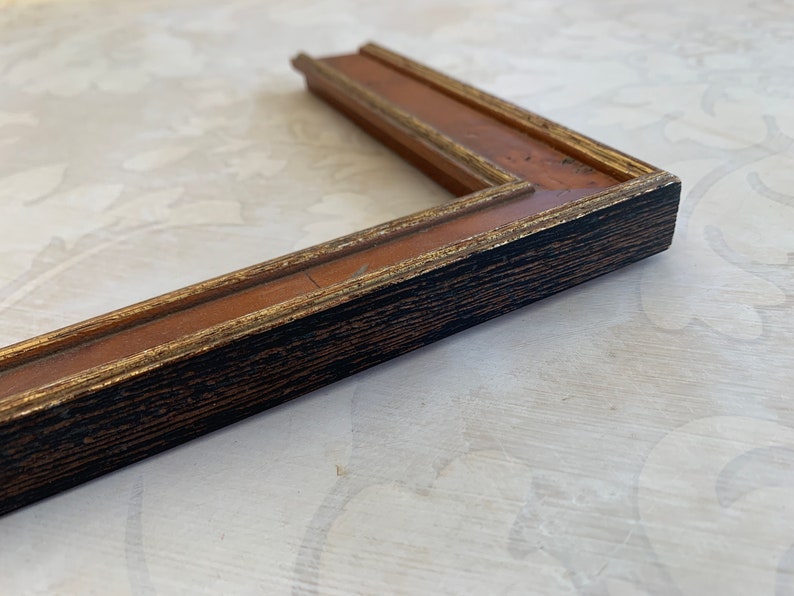 May include: A black and gold picture frame with a wood grain finish. The frame has a simple, classic design.