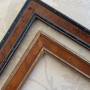 May include: Two picture frames, one with a black and brown wood finish and the other with a gold and brown wood finish.