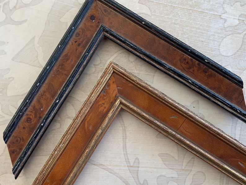 May include: Two picture frames, one with a black and brown wood finish and the other with a gold and brown wood finish.