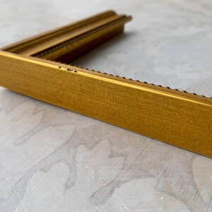 Puede incluir: Un marco de imagen dorado con un borde decorativo de cuentas. El marco est&aacute; hecho de madera y tiene un acabado mate.