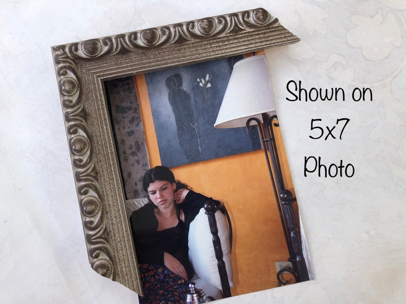 May include: A silver-colored ornate picture frame with a 5x7 photo inside. The photo shows a young woman sitting on a bed with a lamp in the background. The text "Shown on 5x7 Photo" is written in black on a white background.