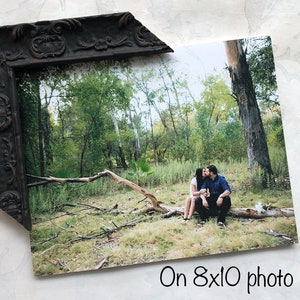May include: A couple kissing whilst sitting on a fallen tree branch in a forest. The photo is printed on an 8x10 photo.