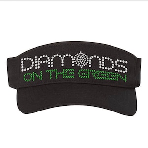 May include: Black visor with the text "Diamonds on the Green" in white rhinestones and green rhinestones.