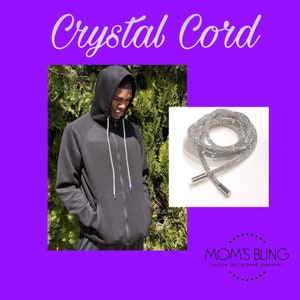 May include: A silver crystal cord shoelace with silver metal tips. The cord is made of a braided rope with crystals embedded in the rope. The cord is displayed on a white background. "MOM'S BLING custom decorated apparel!" is written in black text on a white background.
