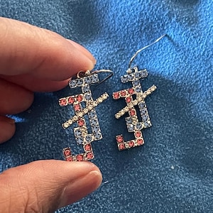 May include: A pair of silver earrings with blue and pink rhinestones. The earrings are shaped like the Chinese character for "joy" or "happiness".