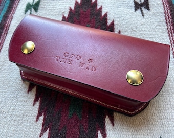May include: A burgundy leather key holder with gold metal accents. The key holder has the text "GPD 4 THE WIN" embossed on the front.