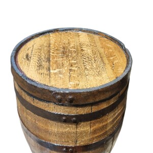 May include: A wooden barrel with a light brown finish, featuring dark metal bands and a matching top. The barrel's staves are visible, and the metal bands are secured with rivets. The barrel is likely used for storage or decoration.