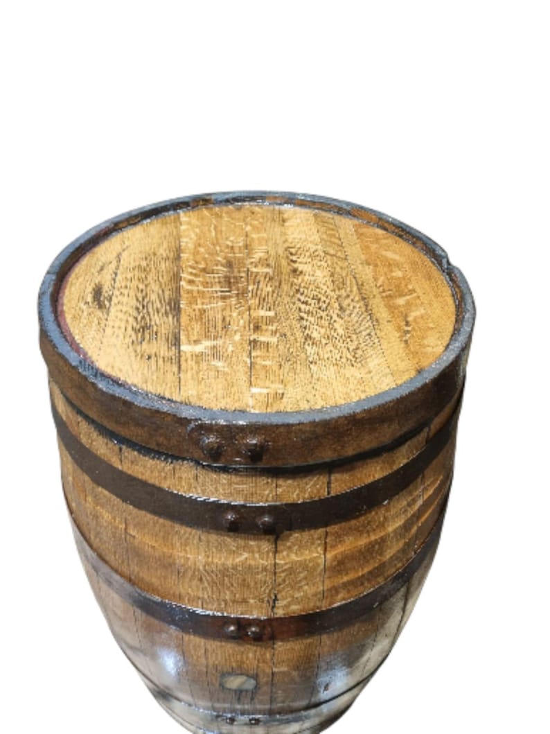May include: A wooden barrel with a light brown finish, featuring dark metal bands and a matching top. The barrel's staves are visible, and the metal bands are secured with rivets. The barrel is likely used for storage or decoration.