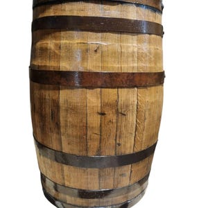 May include: A wooden barrel with a light brown finish, held together by dark metal bands. The barrel has a slightly weathered appearance, suggesting it may have been used for aging or storage. The wood grain is visible.