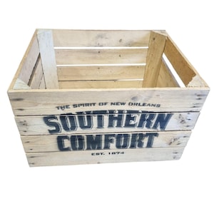 Pode incluir: Uma caixa de madeira r&uacute;stica com as palavras "SOUTHERN COMFORT" e "EST. 1874" impressas em preto. A caixa &eacute; feita de madeira clara e tem uma forma retangular com os lados abertos. O texto "THE SPIRIT OF NEW ORLEANS" est&aacute; impresso acima da marca.