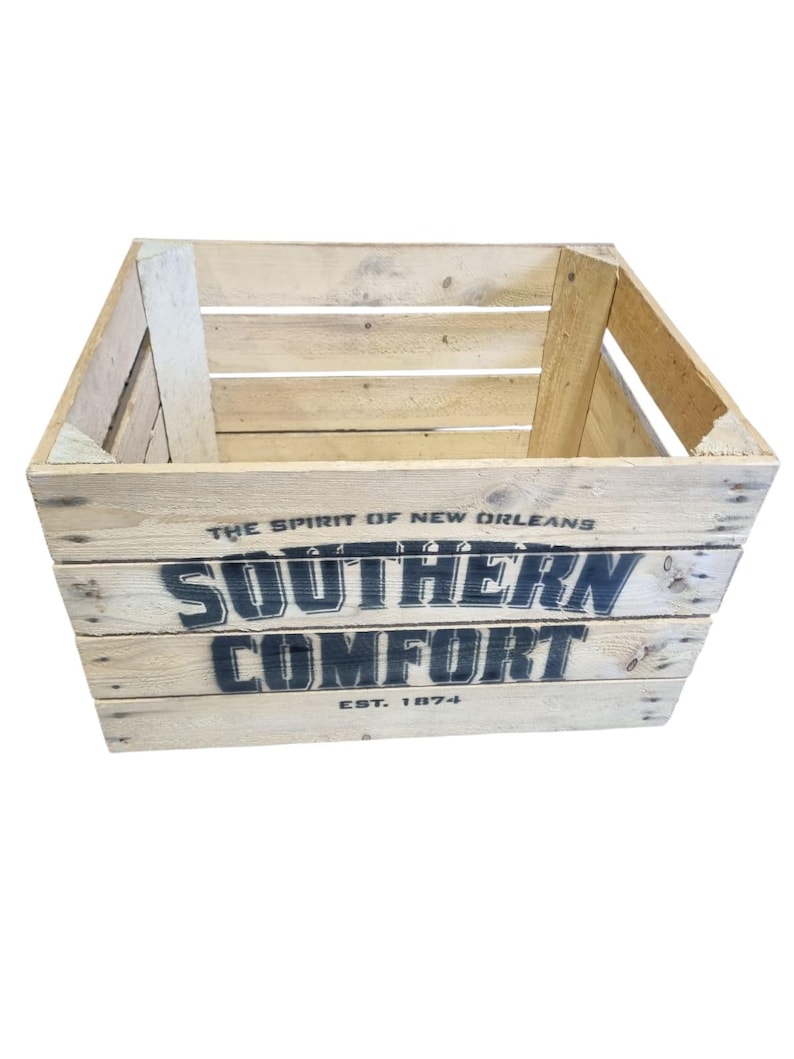 Pode incluir: Uma caixa de madeira r&uacute;stica com as palavras "SOUTHERN COMFORT" e "EST. 1874" impressas em preto. A caixa &eacute; feita de madeira clara e tem uma forma retangular com os lados abertos. O texto "THE SPIRIT OF NEW ORLEANS" est&aacute; impresso acima da marca.