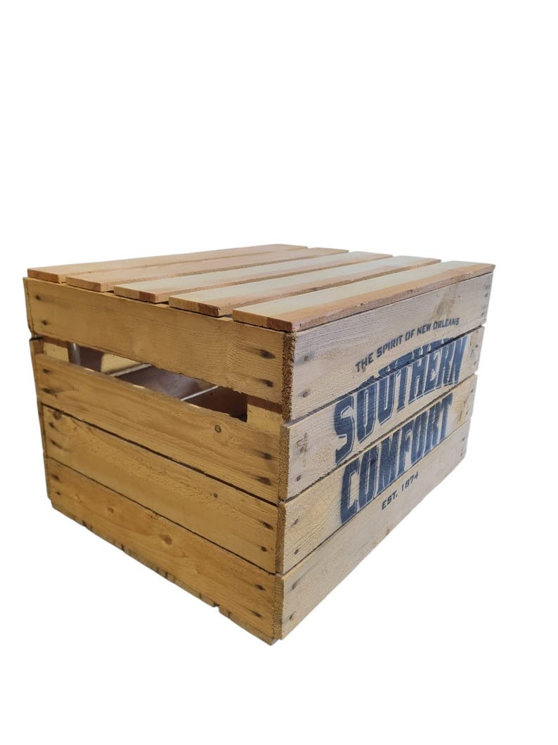 Pode incluir: Caixa de madeira com as palavras "SOUTHERN COMFORT" impressas em azul. A caixa &eacute; feita de madeira castanha clara e tem um topo de ripas. O texto "EST. 1874" tamb&eacute;m &eacute; vis&iacute;vel.