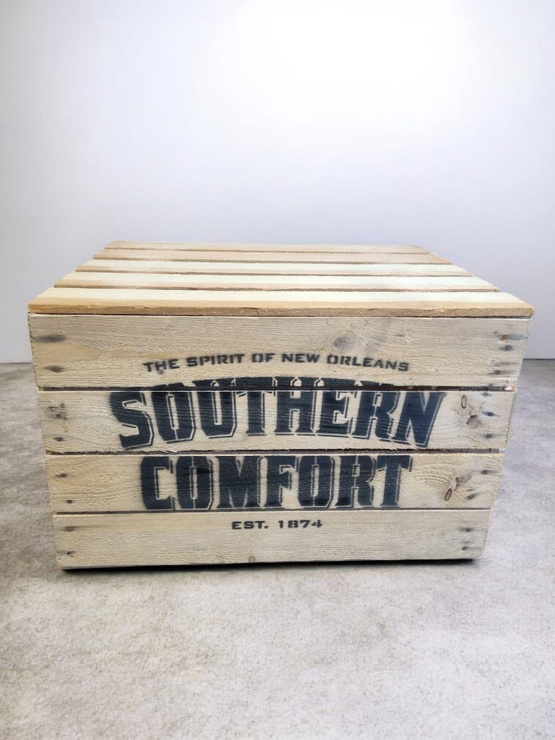 Pode incluir: Uma caixa de madeira com o texto "SOUTHERN COMFORT" em letras pretas. A caixa &eacute; feita de madeira clara e tem a frase "THE SPIRIT OF NEW ORLEANS" e "EST. 1874" impressas.