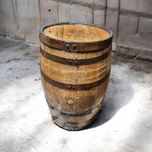 May include: A weathered wooden barrel with dark metal bands. The barrel has a natural wood grain and is slightly tapered. The top and bottom are reinforced with metal rings. The barrel is likely used for storage or decoration.