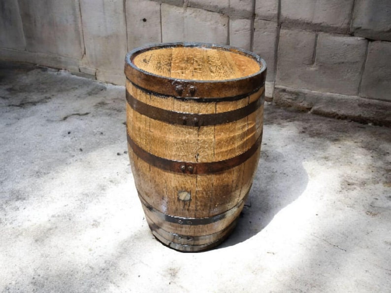 May include: A weathered wooden barrel with dark metal bands. The barrel has a natural wood grain and is slightly tapered. The top and bottom are reinforced with metal rings. The barrel is likely used for storage or decoration.