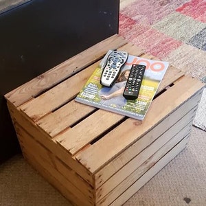 Peut inclure: Une caisse en bois avec un magazine et deux télécommandes sur le dessus. La caisse est en bois naturel et a un aspect rustique. Le magazine est un magazine de style de vie avec une couverture colorée.