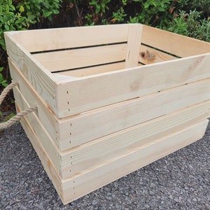 May include: A large, natural wood crate with a rope handle. The crate is made of unfinished pine wood and has a rustic look.