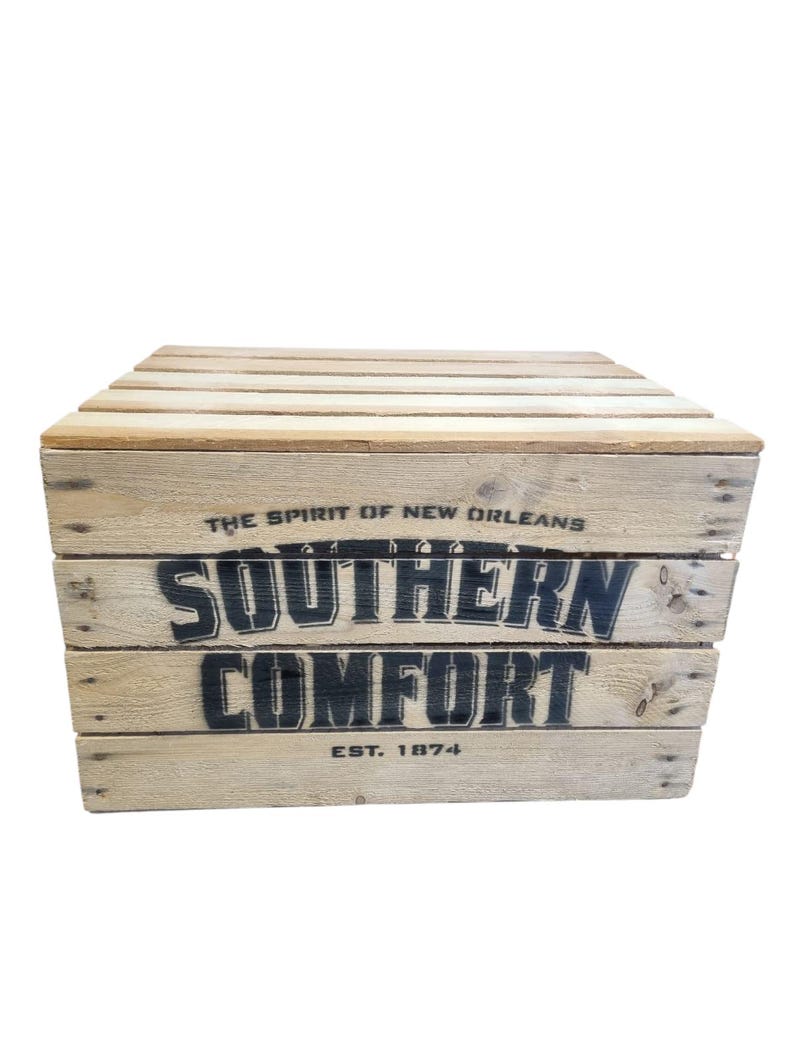 Pode incluir: Uma caixa de madeira com o texto "SOUTHERN COMFORT" em preto, juntamente com "THE SPIRIT OF NEW ORLEANS" e "EST. 1874". A caixa &eacute; feita de madeira clara.