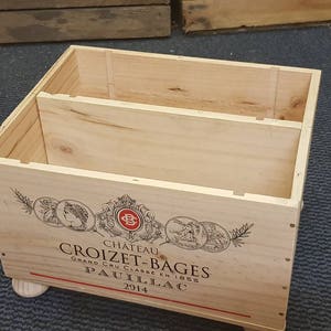 Può includere: Una cassa di vino in legno con un'etichetta che recita "Chateau Croizet-Bages Grand Cru Classe en 1855 Pauillac 2014". La cassa ha due scomparti ed è appoggiata su un tappeto grigio.