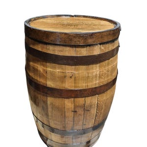 May include: A wooden barrel with a flat top and curved sides. The barrel is made of vertical wooden staves held together by several dark metal bands. The wood has a natural, light brown color with visible grain.