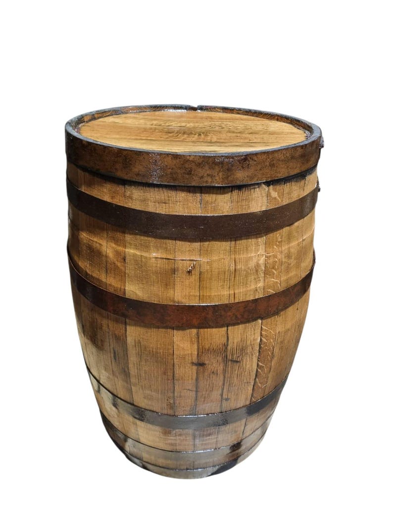 May include: A wooden barrel with a flat top and curved sides. The barrel is made of vertical wooden staves held together by several dark metal bands. The wood has a natural, light brown color with visible grain.