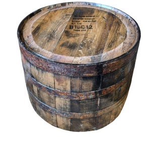 Puede incluir: Un barril de madera envejecida con aros metálicos. La parte superior del barril tiene el texto "BEAM BRANDS U.S. BOURBON WHISKEY" y "B18C12 TANK 224". El barril es marrón con marcas oscuras.