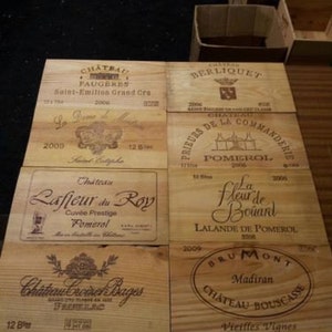Può includere: Una collezione di sei cassette di legno per vino con etichette che mostrano i nomi di diverse cantine francesi. Le cassette sono tutte in legno marrone chiaro e hanno un aspetto rustico. Le etichette sono stampate in inchiostro nero e includono i nomi delle cantine, i vitigni e gli anni di vendemmia. Le cassette sono disposte in due file di tre.