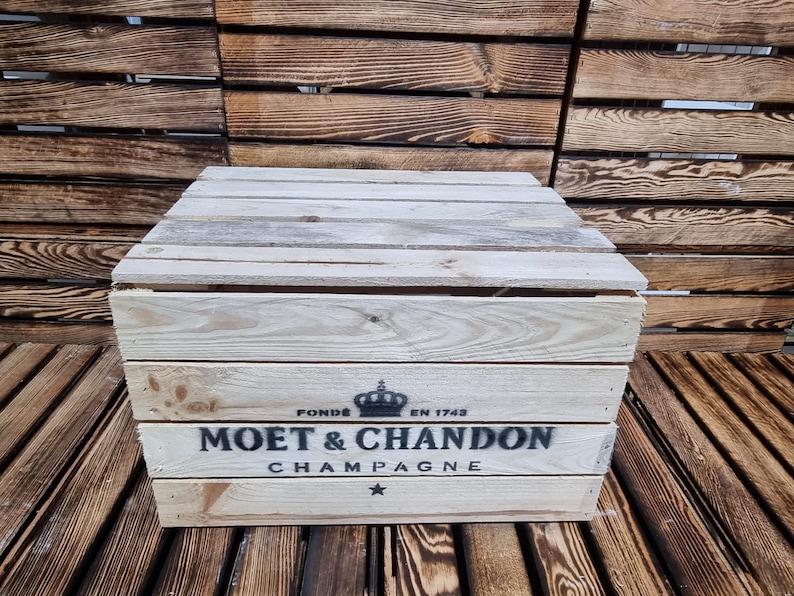 以下が含まれることがあります： 前面に「Mo&euml;t＆Chandon Champagne」と印刷された木製の箱。箱は明るい木で作られており、濃い茶色の染みがあります。箱は木製の表面の上に置かれています。