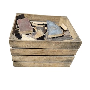 May include: A rectangular wooden crate with horizontal slats containing a collection of assorted scrap wood pieces. The wood fragments vary in size, shape, and color, including light tan, dark brown, and grey tones, filling the open top of the container.