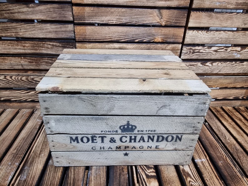 以下が含まれることがあります： 白く塗られた木製の箱で、前面に「Mo&euml;t & Chandon Champagne」と印刷されています。箱は木製の表面の上に置かれています。