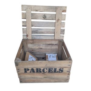 Könnte beinhalten: Eine rustikale Holzkiste mit dem Wort "PARCELS" in schwarzer Schrift auf der Vorderseite. Der Deckel ist geöffnet und zeigt zwei Pakete im Inneren. Die Kiste besteht aus verwittertem Holz, was auf eine Vintage- oder Upcycling-Ästhetik hindeutet.